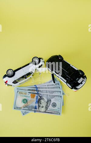 Deux voitures jouets blanches et un dollar américain sur fond jaune. Image d'un accident de la route. Concept d'assurance automobile et accident de voiture. Banque D'Images