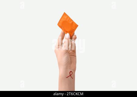 Main féminine avec préservatif et signe de ruban rouge sur fond blanc. Concept de la Journée du sida Banque D'Images