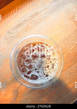 Une tasse d'Americano glacé avec des glaçons placé sur une table en bois dans un café. Vue de dessus d'un verre de café à la lumière du soleil du matin Banque D'Images