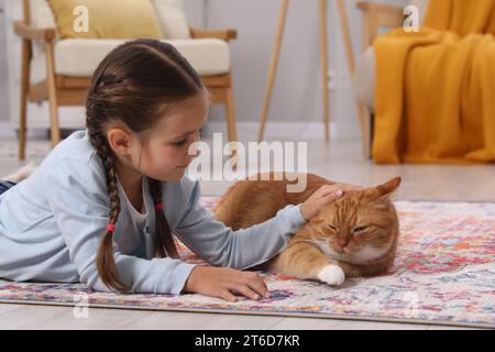 Petite fille caressant chat mignon gingembre sur tapis à la maison Banque D'Images