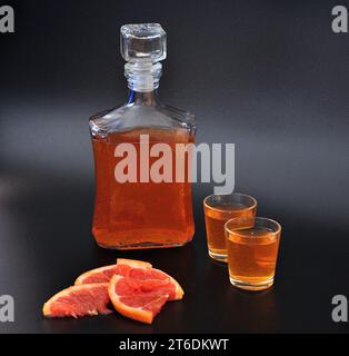 Liqueur de pamplemousse sur fond noir, une bouteille et deux verres avec de l'alcool fort et des morceaux d'agrumes mûrs. Gros plan. Banque D'Images