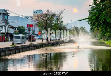 Sprinklers pulvériser de l'eau sur le plan d'eau entourant le périmètre de la vieille ville de la capitale nord de la Thaïlande City.Sun couchant au-dessus de la tumulta fumée Banque D'Images