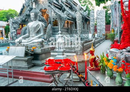 Tables avec des fleurs rouges et oranges, guirlandes sacrées, bougies allumées, statues et encens, devant l'un des plus beaux temples de Chiang Mai.unique structu Banque D'Images