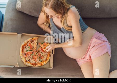 Une femme enceinte apprécie une tranche de pizza, savourant un moment de plaisir tout en satisfaisant son envie d'un régal délicieux et réconfortant. Excité Banque D'Images