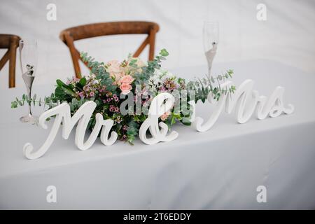 Table pour les amoureux en gros plan - nappe blanche avec garniture florale rustique, flûtes à champagne et pancarte MR & Mrs Banque D'Images