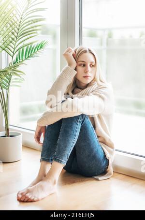 Fille triste près de la fenêtre pensant à quelque chose. Une dame stressée se sent seule Banque D'Images