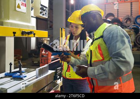 Deux personnes sont occupées à faire fonctionner une machine de grande taille dans un environnement d'usine animé. Banque D'Images