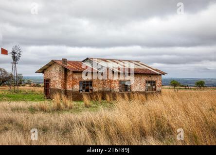 ancienne maison de ferme en ruine avec un moulin à vent vintage haute herbe sèche au premier plan Banque D'Images