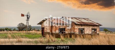 ancienne maison de ferme en ruine avec un moulin à vent vintage haute herbe sèche au premier plan Banque D'Images