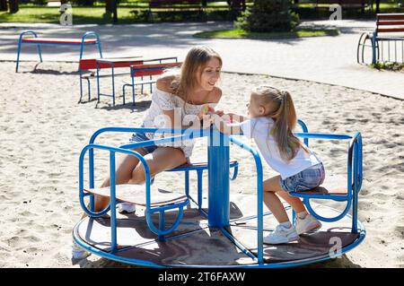 Mère et fille jouent sur l'aire de jeux dans le parc de la ville d'été. Enfance, loisirs et concept de personnes - repos familial heureux et passer un bon moment Banque D'Images