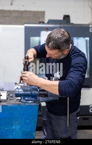 Homme professionnel travaillant sur une pièce d'acier avec marteau dans un atelier d'usine de métal. Mécanique industrielle et réparations Banque D'Images