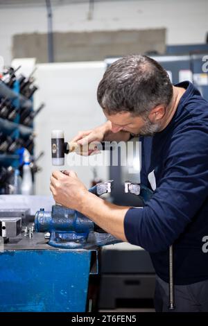 Homme professionnel travaillant sur une pièce d'acier avec marteau dans un atelier d'usine de métal. Mécanique industrielle et réparations Banque D'Images