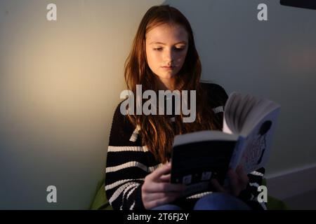 Adolescente feuilletant un livre de lecture, ya roman, saisi par l'histoire, tournant les pages Banque D'Images