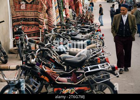 Un vieil homme portant un fès passe devant une rangée de motos (cyclomoteurs). Banque D'Images