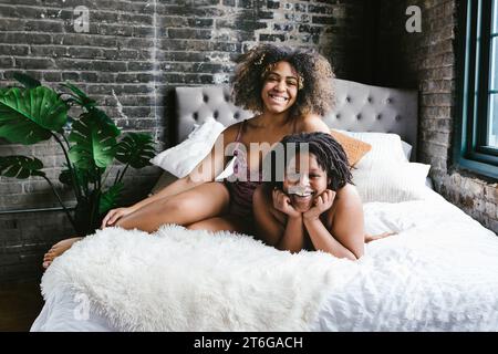 Deux danseuses de race mixte sourient ensemble sur le lit dans l'appartement Banque D'Images