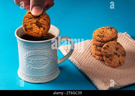 Un homme jetant un biscuit aux pépites de chocolat dans une tasse de café noir Banque D'Images