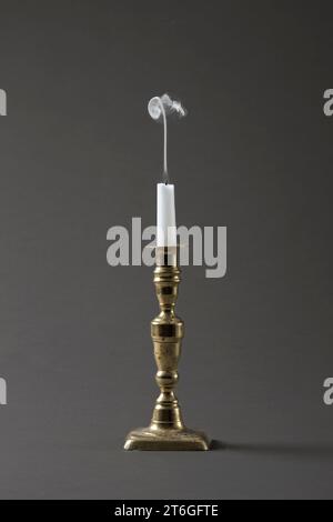 Un brin de fumée s'élevant d'une bougie récemment éteinte (snoffed) dans un vieux chandelier en laiton, sur un fond de studio gris Uni Banque D'Images