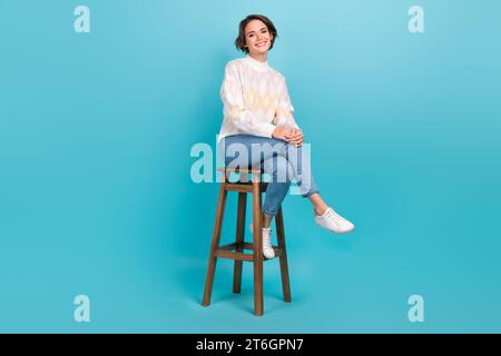 Plein corps cadre de fille attrayante joyeuse assise en bois chaise confortable pub atmosphère de relaxation isolé sur fond de couleur bleue Banque D'Images