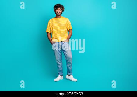 Photo pleine longueur de joli jeune homme posant promo shopping habillé élégant vêtement jaune rayé isolé sur fond de couleur cyan Banque D'Images