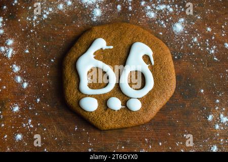 Un biscuit sucré en pain d'épice recouvert de glaçage blanc sous la forme du numéro 66 repose sur une vieille planche entourée de farine Banque D'Images