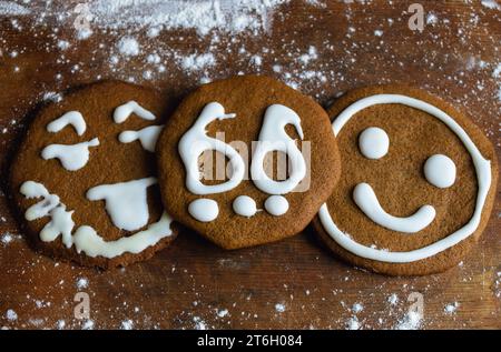 Trois biscuits sucrés recouverts de glaçage blanc sous forme d'émoticônes et le numéro 66 reposent sur une vieille planche entourée de farine Banque D'Images