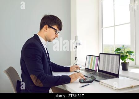 Jeune comptable professionnel utilise la calculatrice pour l'audit d'entreprise se trouve à la table de bureau avec des ordinateurs portables Banque D'Images