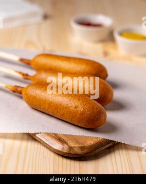 Chiens de maïs frits sur papier parchemin avec du ketchup et de la moutarde en arrière-plan avec des serviettes Banque D'Images