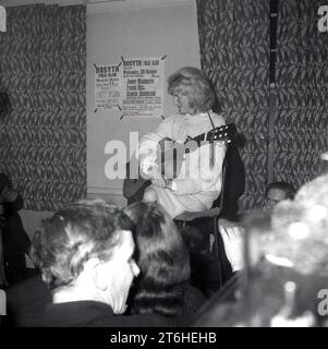 Vers la fin des années 1960, historique, une chanteuse folk assise dans une pièce avec guitare. Coincé sur le mur derrière elle, des avis pour la soirée d'ouverture du Rosyth Folk Club à l'Hôtel Rosyth, Angleterre, Royaume-Uni, déclarant qu'il mettra en vedette des chanteurs ; Jimmy Macbeath, Paddie Bell, Hamish Henderson le 20 octobre, avec Tregullion Jack & Barbara & invités, avec la semaine suivante Matt McGinn sur scène. Banque D'Images