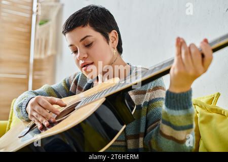 jeune femme concentrée en tenue décontractée jouant de la guitare sur la leçon de musique à distance, l'éducation à la maison Banque D'Images