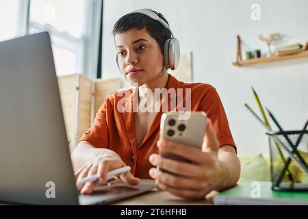 jeune étudiant attrayant étudiant à son ordinateur portable avec téléphone portable et stylo dans les mains, l'éducation Banque D'Images