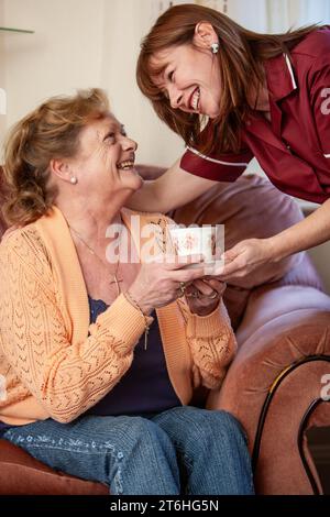 Aider les personnes âgées : soins à domicile. Un sourire éclatant et une tasse de thé de bienvenue pour une dame aînée de sa soignante. À partir d'une série d'images associées. Banque D'Images
