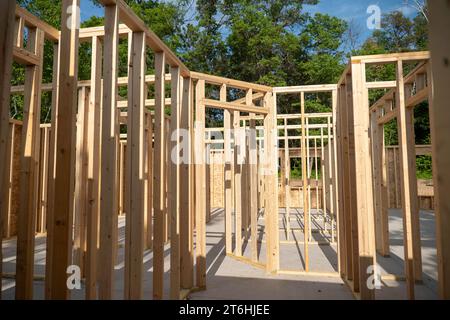 Gros plan des poteaux de charpente en bois au nouveau chantier de construction de maison au soleil avec des ombres, avec des arbres en arrière-plan. Banque D'Images