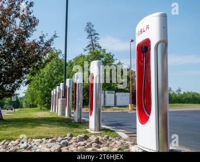 BEMIDJI, MN – 3 JUIN 2023 : une rangée de stations de recharge Tesla Supercharger près de l'herbe verte et des arbres et un ciel bleu dans le Minnesota. Banque D'Images