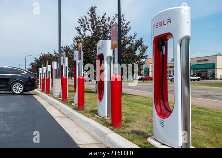 BEMIDJI, MN – 3 JUIN 2023 : une rangée de stations de recharge Tesla Supercharger près de la rue avec une voiture électrique noire branchée pour la recharge. Banque D'Images