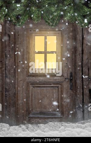 Porte avec fenêtre éclairée dans une cabane de montagne enneigée avec des branches de sapin Banque D'Images