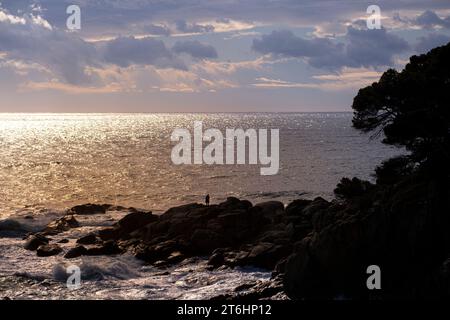 Silhouette d'un homme sur quelques rochers sur la côte de la Costa Brava dans la province de Gérone en Espagne au coucher du soleil Banque D'Images