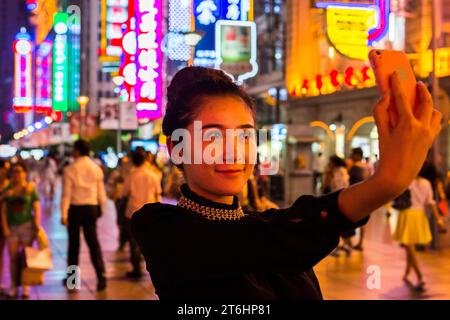 Chine, Shanghai, le Nanjing Dong lu la nuit, femme chinoise faisant un selfy Banque D'Images