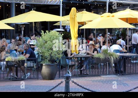 Un groupe de personnes dînant en plein air sous des parasols jaunes dans un cadre contemporain Banque D'Images
