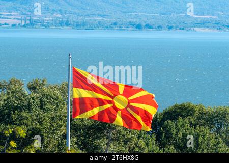 Drapeau macédonien, sur le poteau d'argent agitant au-dessus des arbres. Dojran Lake.as background. Temps venteux. Patrie du soleil. République de Macédoine. Banque D'Images