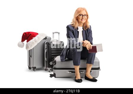 Femme assise sur une valise tenant un passeport et un billet pour une destination de noël isolé sur fond blanc Banque D'Images