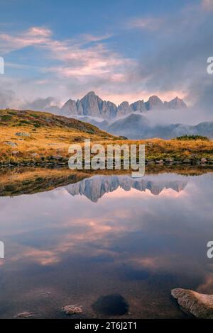 Italie, Vénétie, quartier de Belluno, Falcade, coucher de soleil brumeux en automne avec le côté nord de la Pale di San Martino reflété sur un étang alpin, Dolomites Banque D'Images