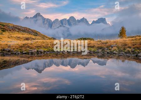 Italie, Vénétie, quartier de Belluno, Falcade, coucher de soleil brumeux en automne avec le côté nord de la Pale di San Martino reflété sur un étang alpin, Dolomites Banque D'Images