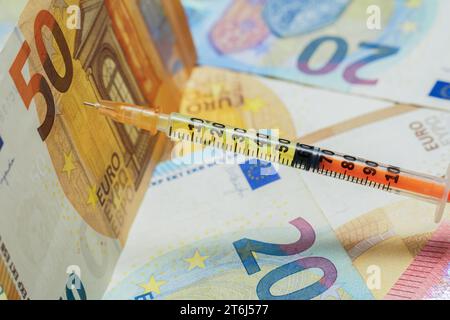 Seringue remplie de liquide jaune avec l'aiguille collée dans un concept de coûts de soins de santé de billets de 50 euros Banque D'Images