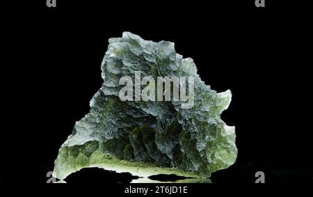 Pierre moldavite isolée sur fond noir. Gros plan d'une pierre précieuse tchèque verte. Véritable verre de tektite naturel. Banque D'Images