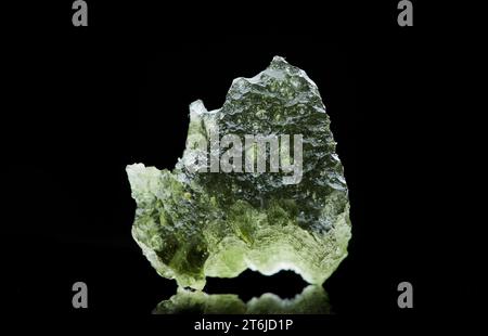 Pierre moldavite isolée sur fond noir. Gros plan d'une pierre précieuse tchèque verte. Véritable verre de tektite naturel. Banque D'Images