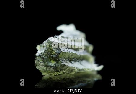 Pierre moldavite isolée sur fond noir. Gros plan d'une pierre précieuse tchèque verte. Véritable verre de tektite naturel. Banque D'Images