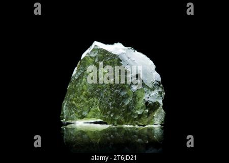 Pierre moldavite isolée sur fond noir. Gros plan d'une pierre précieuse tchèque verte. Véritable verre de tektite naturel. Banque D'Images