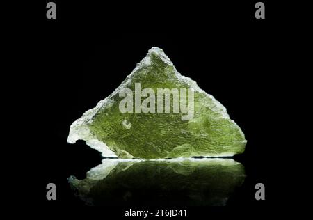 Pierre moldavite isolée sur fond noir. Gros plan d'une pierre précieuse tchèque verte. Véritable verre de tektite naturel. Banque D'Images