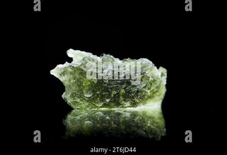 Pierre moldavite isolée sur fond noir. Gros plan d'une pierre précieuse tchèque verte. Véritable verre de tektite naturel. Banque D'Images