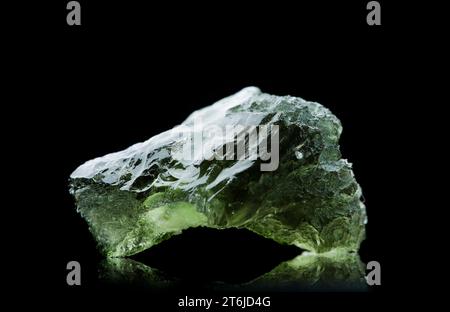 Pierre moldavite isolée sur fond noir. Gros plan d'une pierre précieuse tchèque verte. Véritable verre de tektite naturel. Banque D'Images